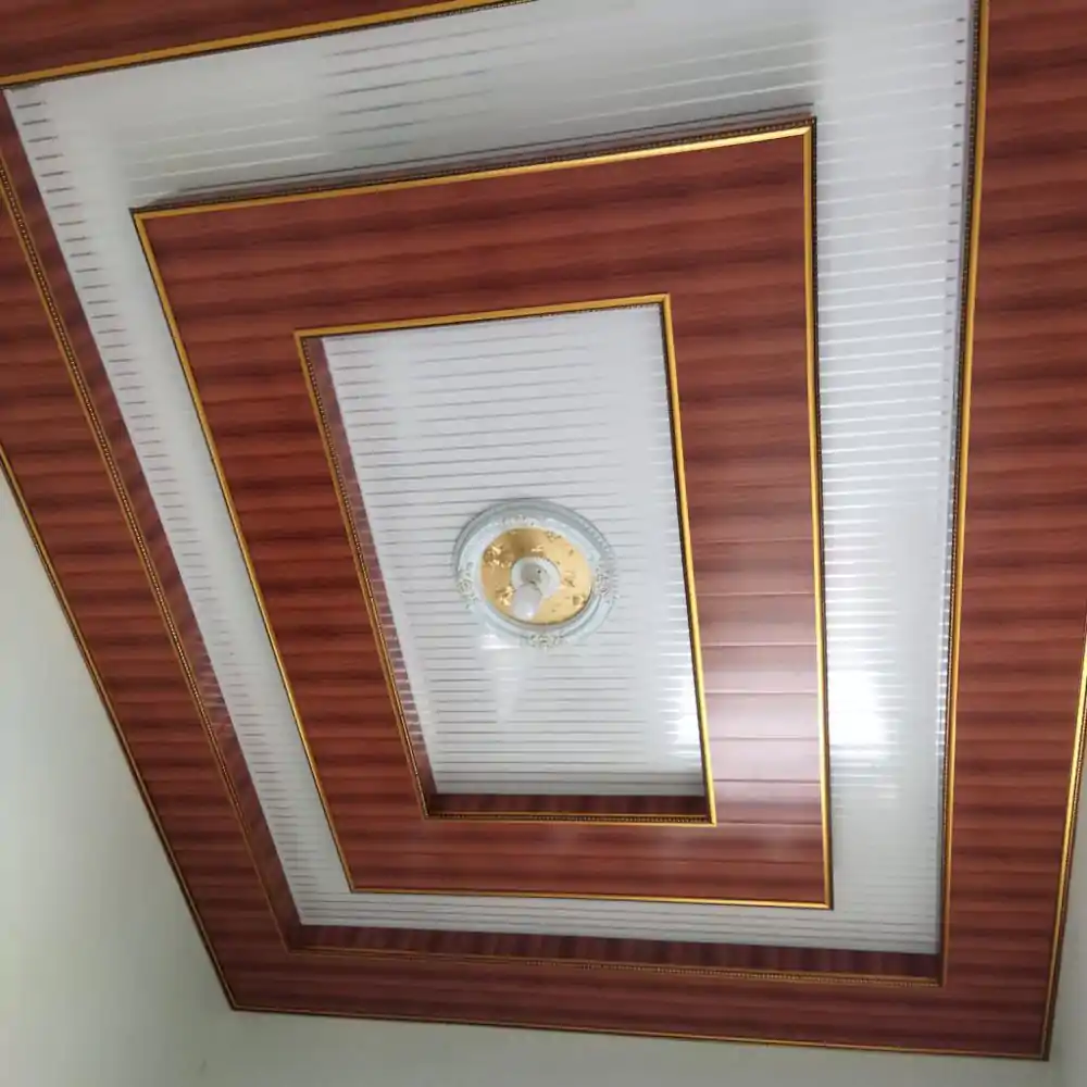 plafon pvc Desain plafon PVC dengan motif kayu dan aksen emas elegan, memberikan sentuhan modern dan mewah pada interior ruangan, cocok untuk aplikasi plafon berkualitas.